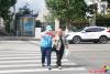 9月18日，在延吉市局子街北大市場(chǎng)西側(cè)的十字路口旁，大學(xué)志愿者劉書達(dá)頭戴志愿者標(biāo)志帽、身穿藍(lán)馬甲、佩戴綬帶和袖標(biāo)，手拿小紅旗，在路口維護(hù)交通秩序，引導(dǎo)行人通過(guò)斑馬線安全過(guò)馬路。